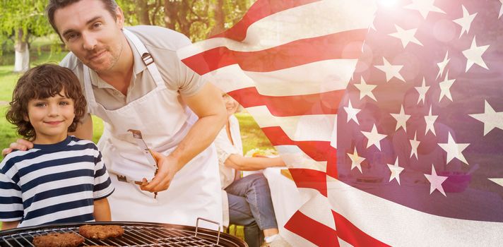 Father and son at barbecue grill with family having lunch in park against focus on usa flag