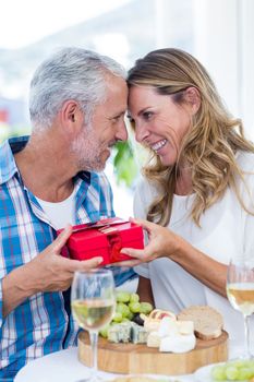 Romantic mature couple holding gift while sitting by table in restaurant