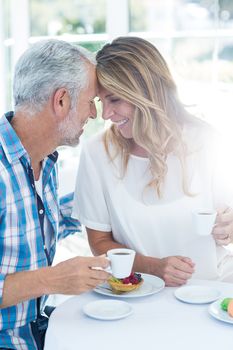 Happy romantic mature couple holding coffee cup at table in restaurant