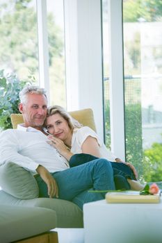 Portrait of romantic mature couple sitting on armchair at home