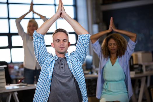 Businessman practicing yoga with coworkers in creative office