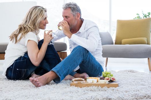 Romantic couple drinking white wine while sitting on rug at home