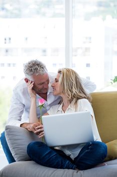 Romantic mature couple with rose and laptop at home