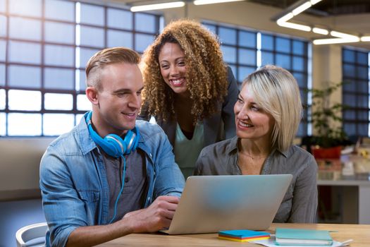 Happy creative business people discussing over laptop at desk in office