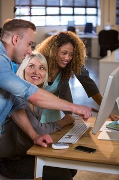 Happy creative business people discussing over computer at desk in office