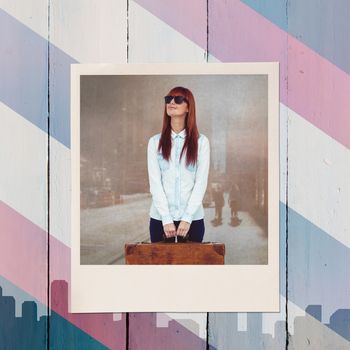 Smiling hipster woman holding suitcase against colored background