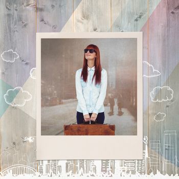 Smiling hipster woman holding suitcase against colored wood