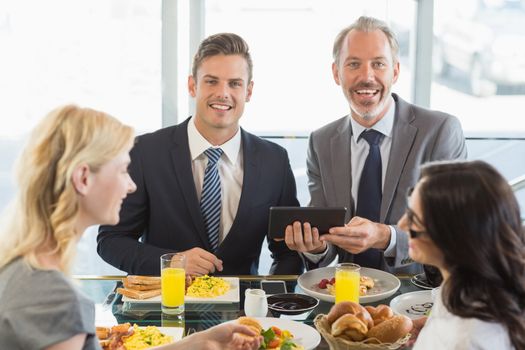 Portrait of business people using digital tablet while having meal in restaurant