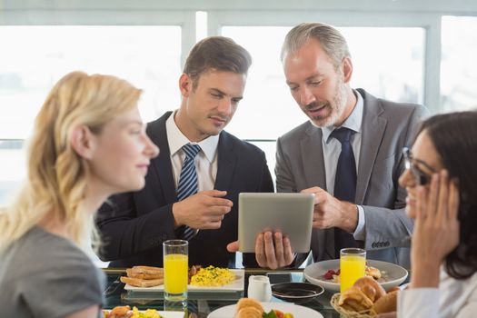Business people using digital tablet while having meal in restaurant