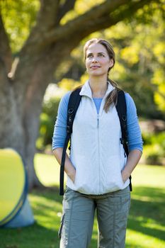 Thoughtful female hiker standing with hands in pockets in forest