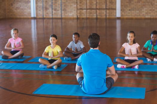 School kids and teacher meditating during yoga class in basketball court at school gym