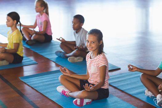 School kids meditating during yoga class in basketball court at school gym