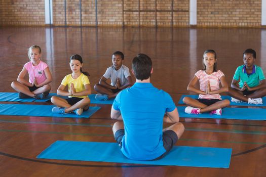 School kids and teacher meditating during yoga class in basketball court at school gym