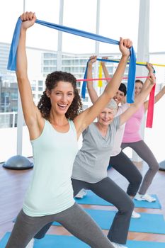 Happy female trainer with class holding up exercise belts at yoga class