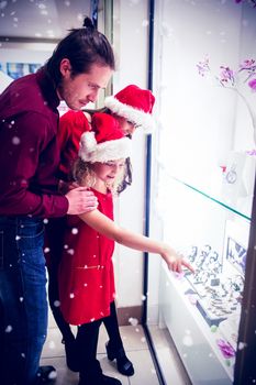 Family in Christmas attire looking at display of wrist watch against snow falling