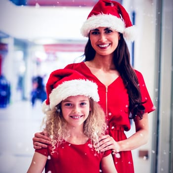 Portrait of mother and daughter in Christmas attire standing with gifts against snow falling