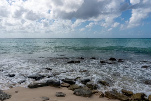Panorama of the Caribbean Sea from the shore covered with large stones that break the waves

