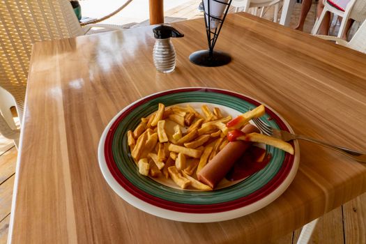Fried fries, sausage and ketchup in a plate with red and green stripes in a roadside cafe