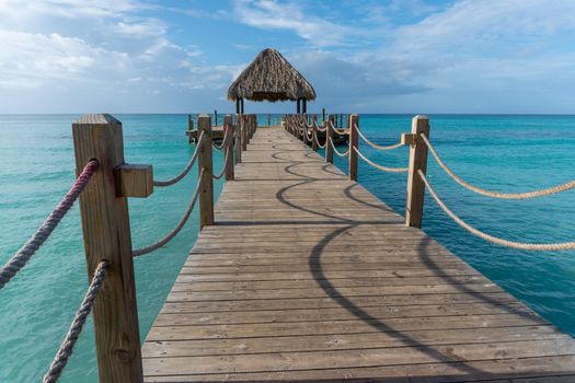 A long wooden bridge leads into the sea to the observation deck with a wooden canopy of palm leaves

