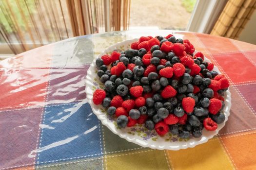 A plate, with fresh raspberries and blueberries, lies on a table covered with oilcloth

