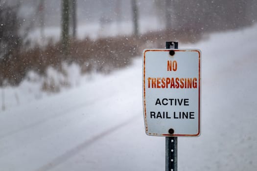 On a snowy day in winter, a sign placed at the intersection of railroad tracks and a footpath reads, "No Tresspassing: Active Rail Line", warning pedestrians not to wander onto the tracks.