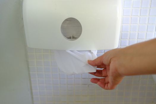 Woman hand taking white paper from holder on wall. Paper towel dispenser. Hygiene concept.  Paper towel dispenser. Hygiene concept.  