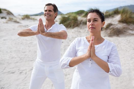 Couple performing yoga on beach during winter