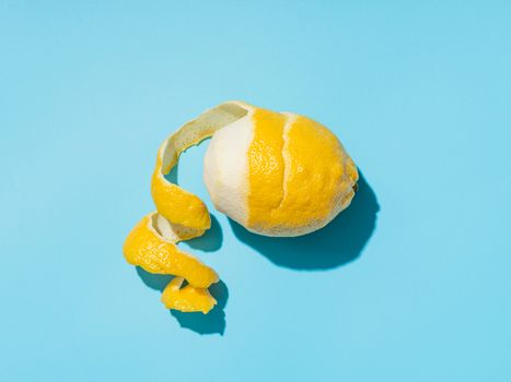 Lemon with spiral peeled zest over blue minimalistic background. Lemon and peel in hard light. Top view or flat lay. Summer minimalistic creative concept and layout