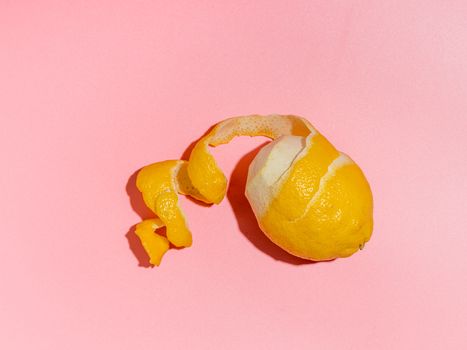 Lemon with spiral peeled zest over pink minimalistic background. Lemon and peel in hard light. Top view or flat lay. Summer minimalistic creative concept and layout