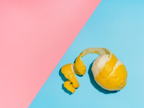 Lemon with spiral peeled zest over blue and pink minimalistic background. Lemon and peel in hard light. Top view or flat lay. Summer minimalistic creative concept and layout. Copy space for text