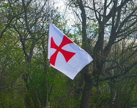 White flag with red cross flying on wind in front of an forest