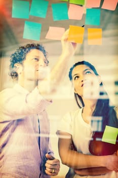 Businessman and businesswoman discussing over adhesive notes on glass wall in office