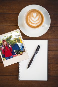 Smiling hipster woman with a travel bag taking selfie against cup of cappuccino with coffee beans on table with copy space