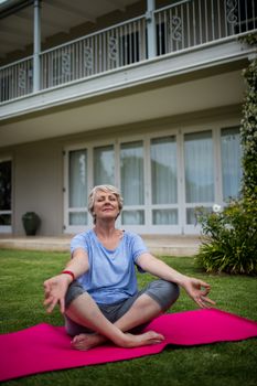 Senior woman practising yoga on exercise mat in lawn
