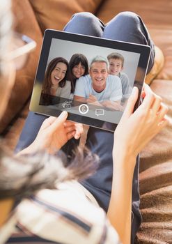 Woman sitting on sofa having video call with family on digital tablet at home