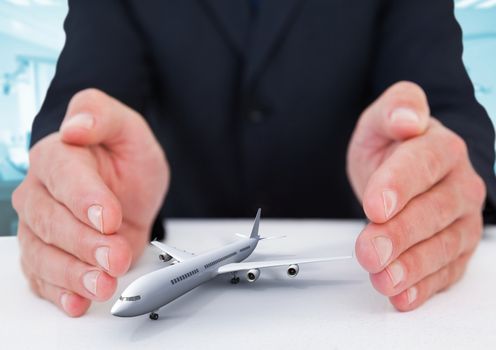 Digital composite image of airplane model surrounded by hands in gesture of protection