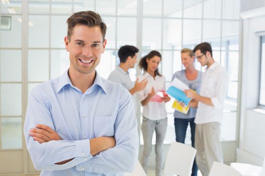 Casual boss smiling at camera in front of his team in the office