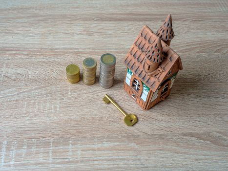 Model of a house, Stack of European Euro coins and golden key On Wooden Table. Real estate agency, mortgage loan, lottery, buying property.Home loan and investment concept. Copy space