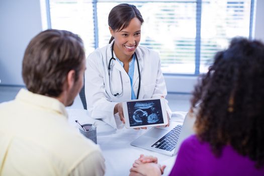 Couple looking at babies ultrasound scan on doctors digital tablet in hospital