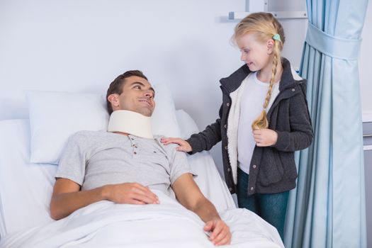 Smiling daughter comforting her sick father in hospital room