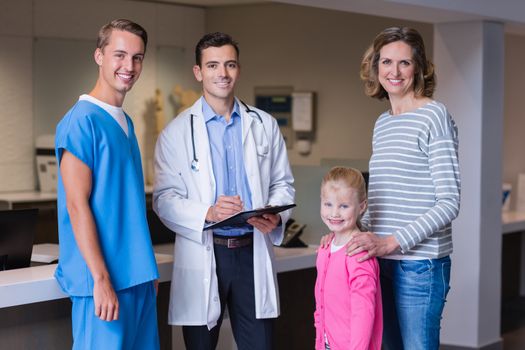 Portrait of doctors discussing medical report with mother and daughter in corridor