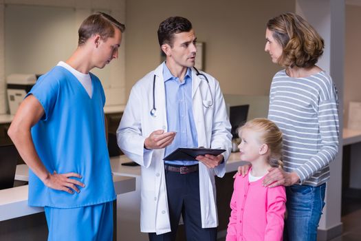 Doctors discussing medical report with mother and daughter in hospital corridor