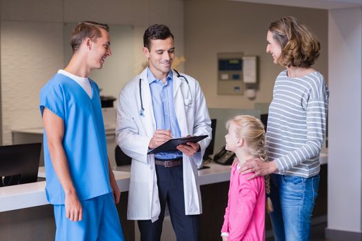 Doctors discussing medical report with mother and daughter in hospital corridor