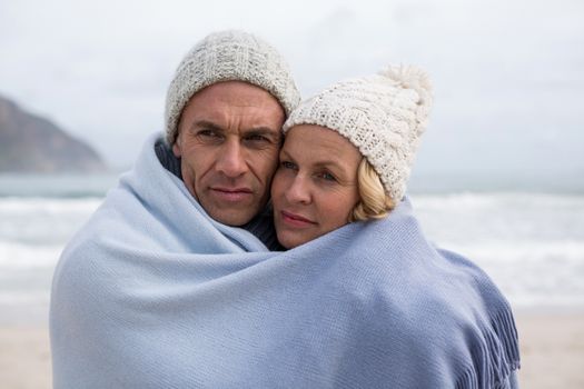 Romantic mature couple wrapped in blanket on the beach