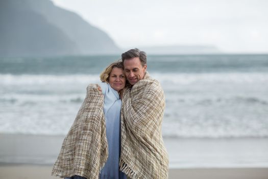 Romantic mature couple wrapped in blanket on the beach