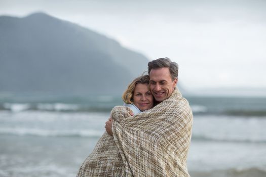 Romantic mature couple wrapped in blanket on the beach