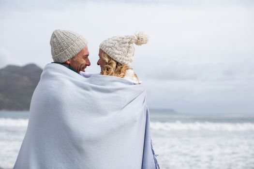 Romantic mature couple wrapped in blanket on the beach