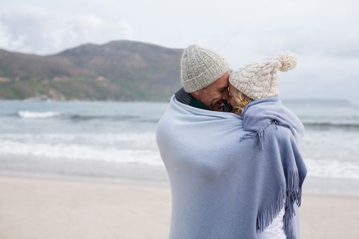 Romantic mature couple wrapped in blanket on the beach