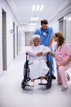 Male and female doctor interacting with female senior patient on wheelchair in corridor at hospital