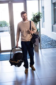 Smiling man holding baby carrier and bag in hospital